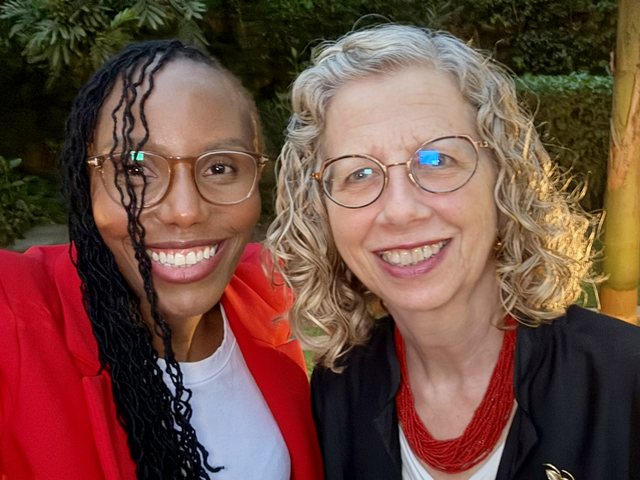 Olivia Otieno in a red blazer taking a selfie with a woman in glasses in a garden