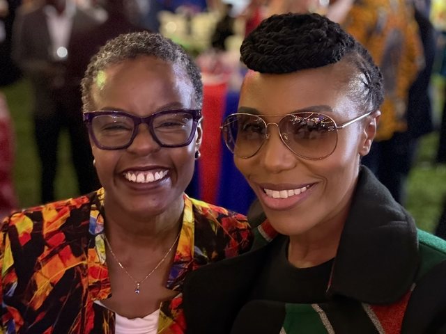 Olivia Otieno in sunglasses and a Kenyan flag scarf laughing with a friend at an evening reception