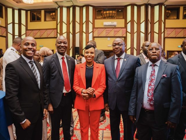 Olivia Otieno in an orange-red suit posing with five men at an event hall