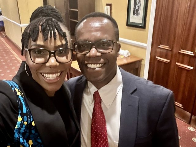 Olivia Otieno taking a selfie with a man in a suit and red tie in a hallway
