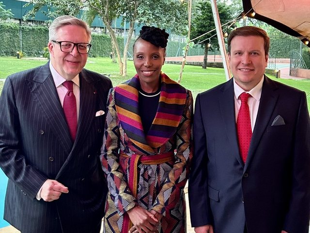 Olivia Otieno in a patterned coat standing between two men at an evening garden reception