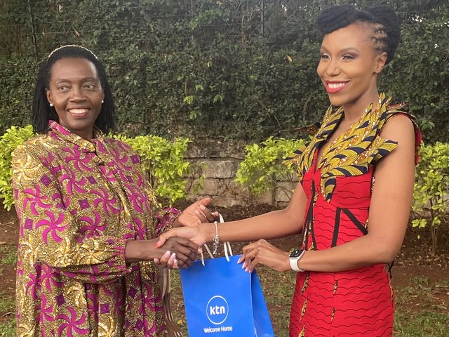 Olivia Otieno in a red African-print dress exchanging a gift bag with a guest in a garden