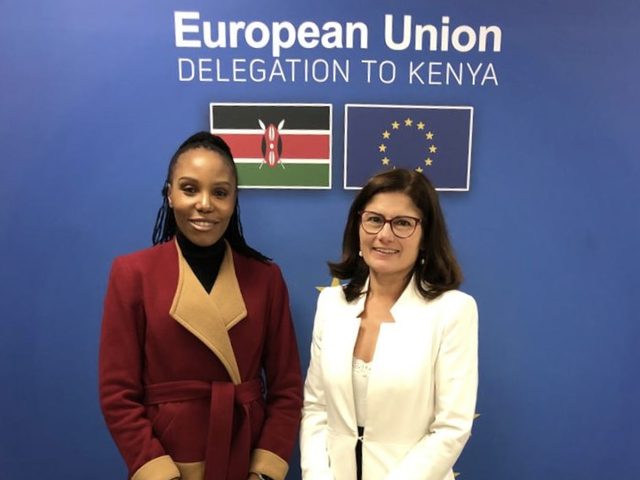 Olivia Otieno standing with a guest in front of the European Union Delegation to Kenya backdrop
