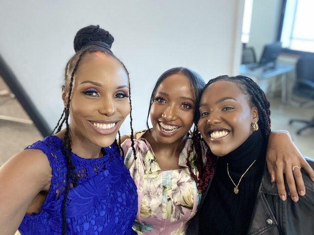 Olivia Otieno in a blue lace dress taking a selfie with two young women