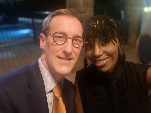 Olivia Otieno taking a selfie with a man in glasses at an evening event