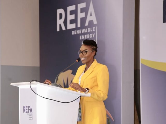 Olivia Otieno in a yellow suit speaking at the Renewable Energy Forum Africa podium