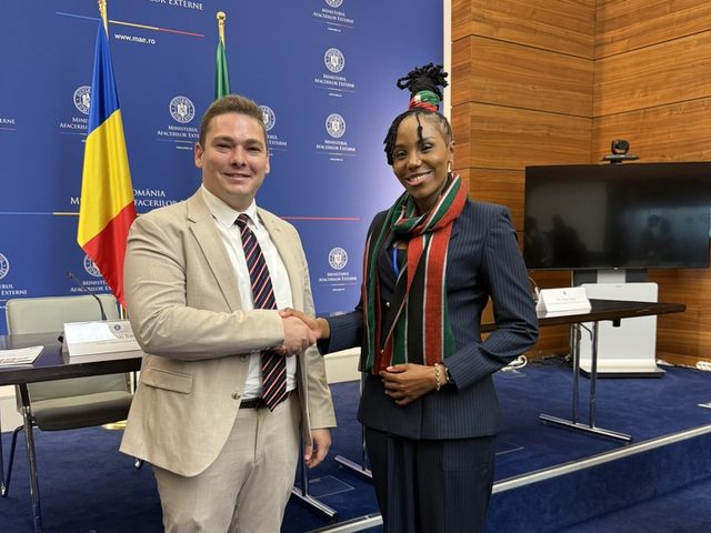 Olivia Otieno shaking hands with an official in front of the Romanian Ministry of Foreign Affairs backdrop