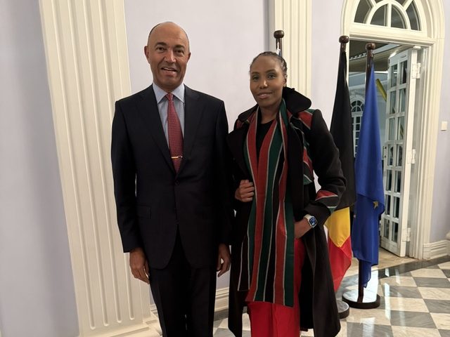 Olivia Otieno standing with a diplomat beside the Belgian and European Union flags
