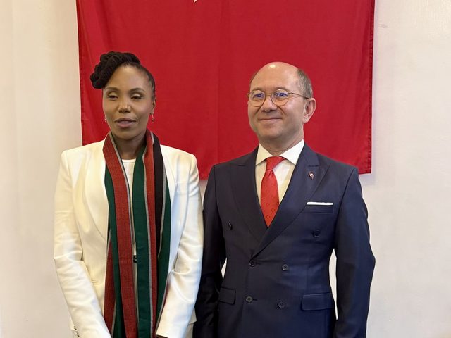 Olivia Otieno standing with a diplomat in front of a Turkish flag