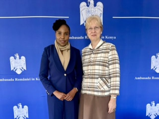 Olivia Otieno with a guest in front of the Embassy of Romania in Kenya backdrop