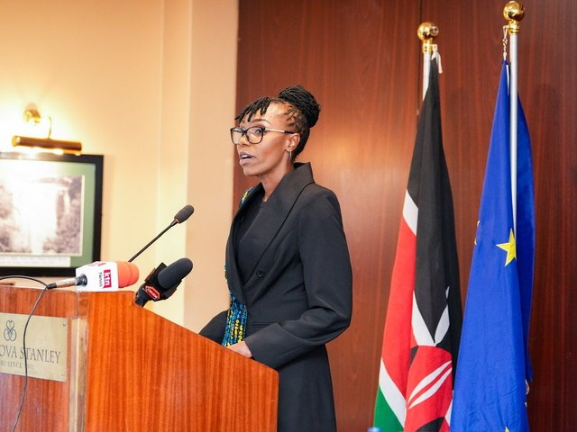Olivia Otieno in a black suit speaking at a podium beside the Kenyan and European Union flags